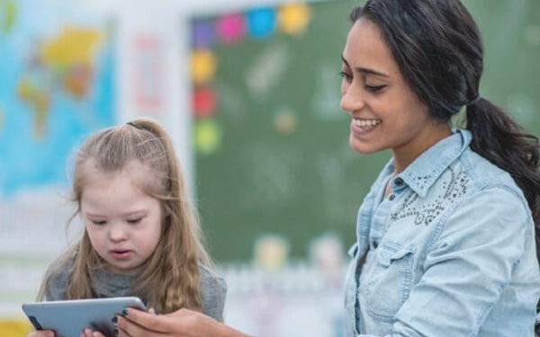 Teacher smiling as young student focuses on a phone or small tablet